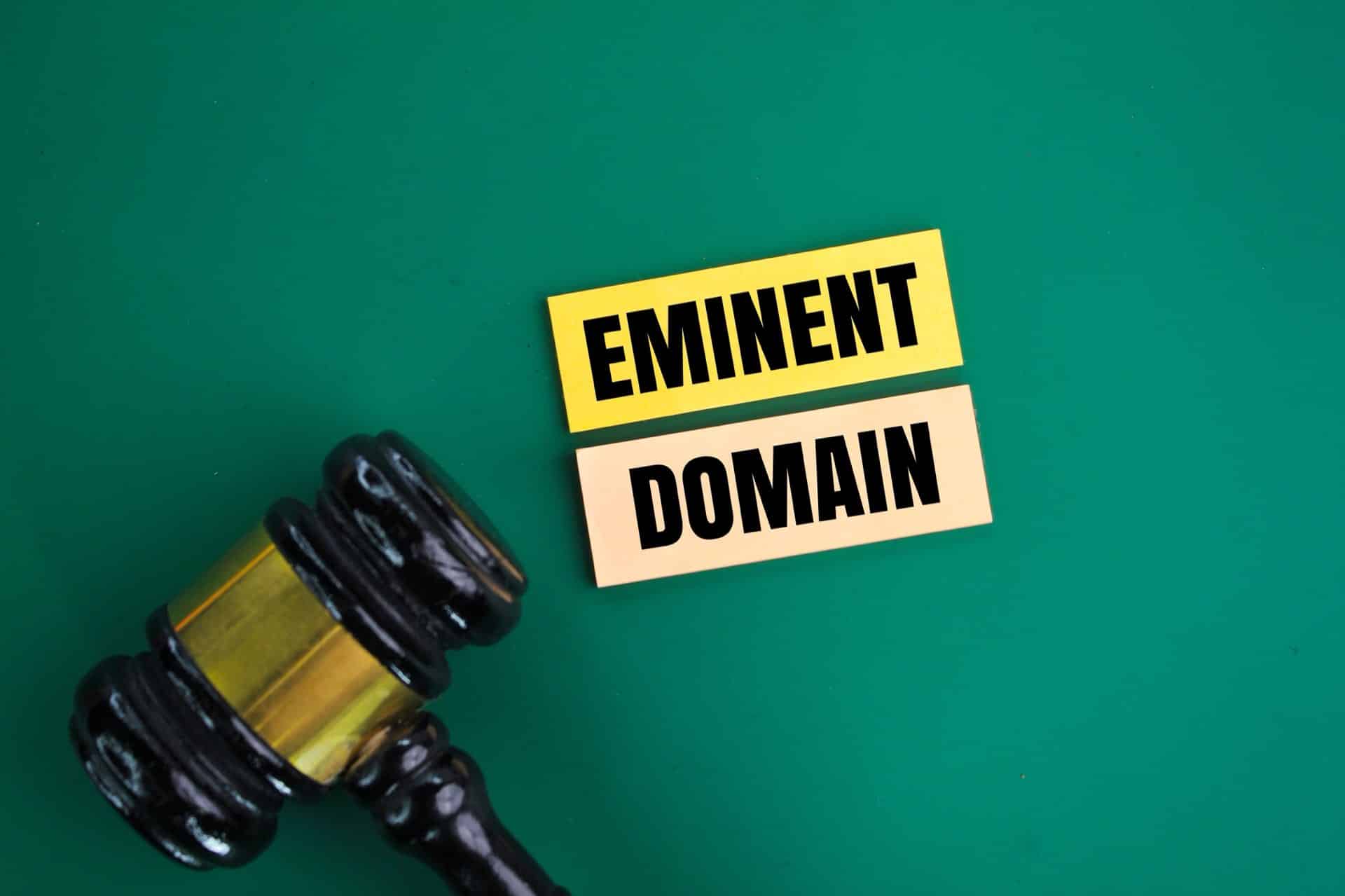 Judge's Gavel next to yellow colored paper that says eminent domain on green background
