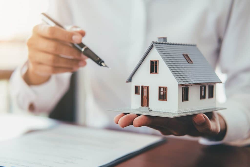 Real estate agent holds a pen & house model | Sewell Sewell Beard LLC