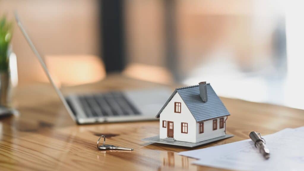 Tiny model home next to a sheet of paper and computer