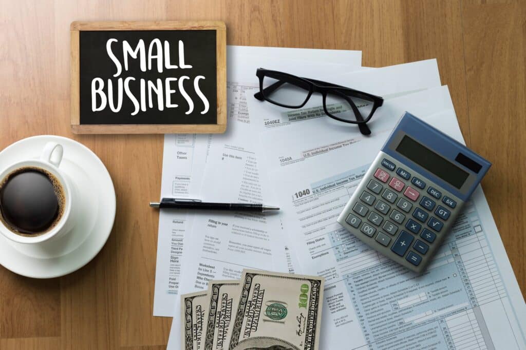Pile of papers with a calculator, glasses, money and a pen on top of it next to a sign that says small business