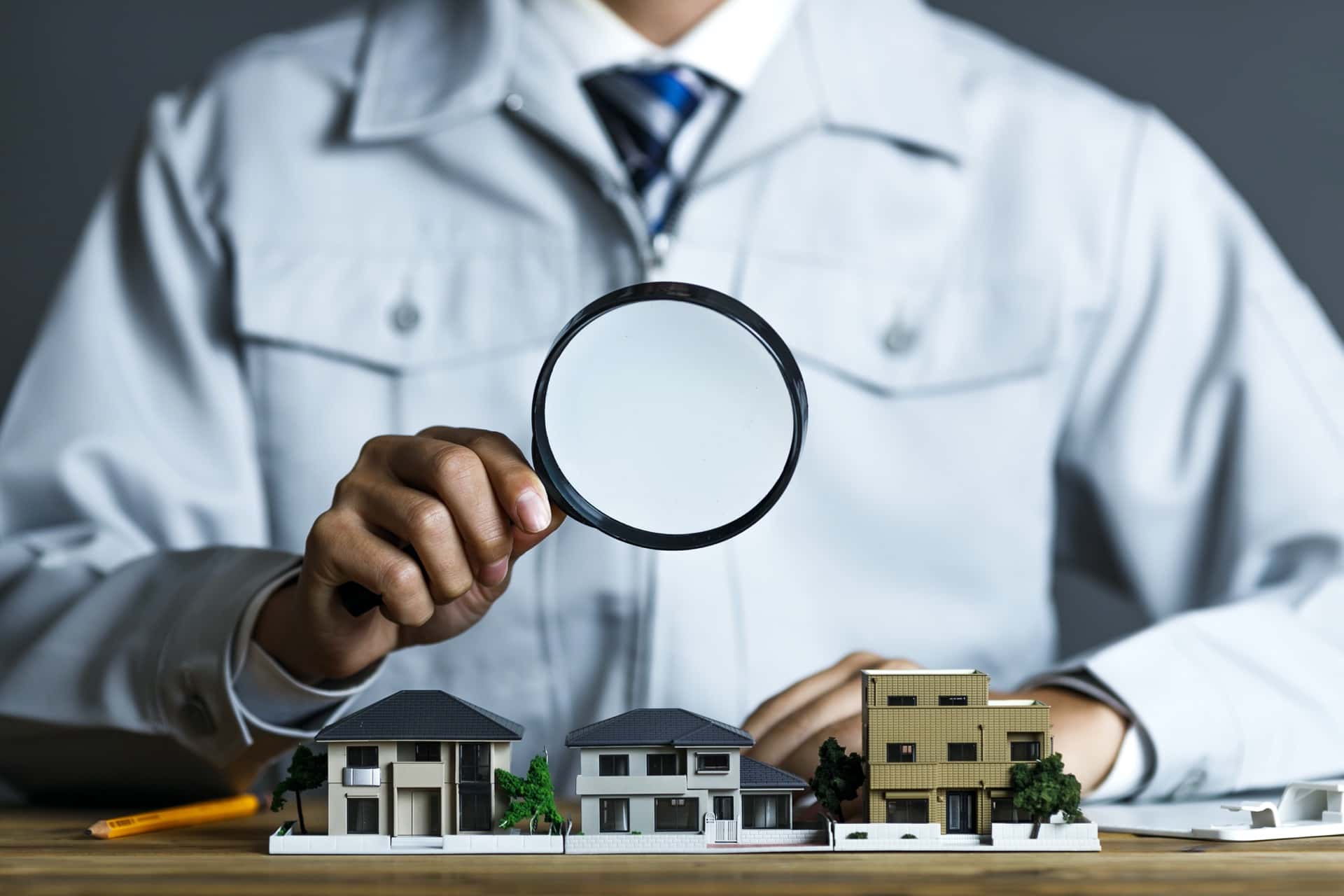 A man in white coat holding magnifying glass up to small model homes