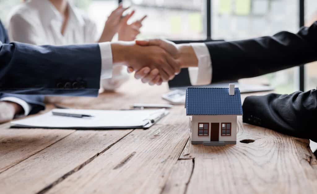 Two business professionals shaking hands over a model house | Sewell Sewell Beard LLC