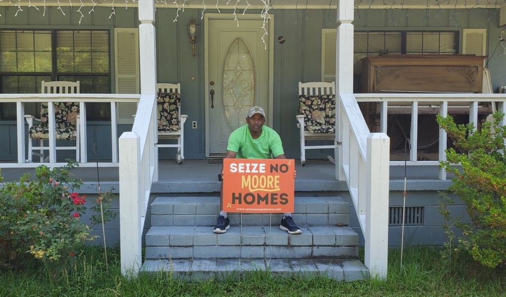 A man sits on a porch holding a sign | Sewell Sewell Beard LLC