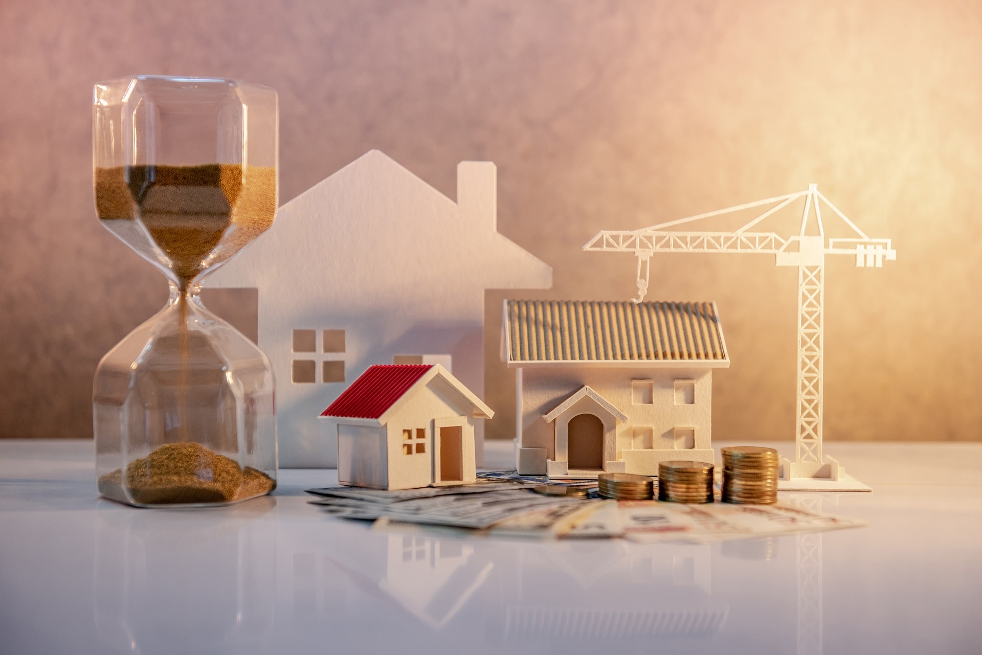 Coin stack on international banknotes with hourglasses, house and crane models on the table.