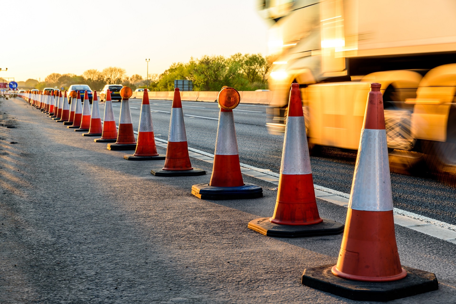 Construction vehicle drives past long line of roadwork cones